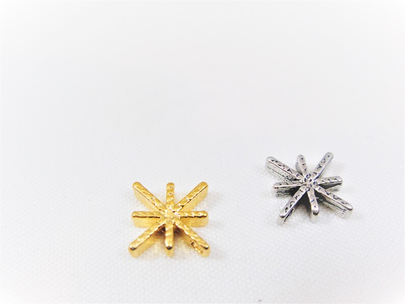 May include: Two star-shaped charms, one gold and one silver. Both charms have a textured surface and eight points.