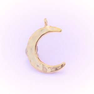 May include: A gold crescent moon charm pendant. The pendant has a hammered texture and a smooth, polished finish.
