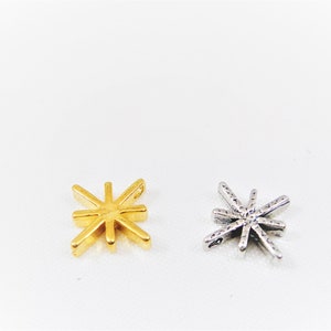 May include: Two star-shaped charms, one gold and one silver. Both charms have a detailed design with multiple points.
