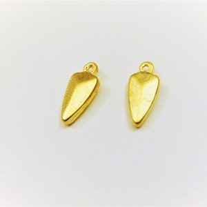 Puede incluir: Dos colgantes de metal de color dorado en forma de lágrima puntiaguda.