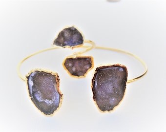 May include: A gold bangle bracelet featuring three purple agate stones. The stones are set in gold and have a rough, natural texture.