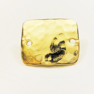 May include: A gold-colored, hammered metal tag with two holes. The tag is rectangular and has an irregular shape.