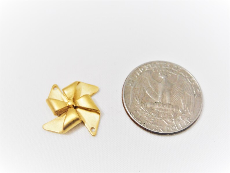 May include: Gold-colored metal bow charm with a swirl design. The charm is about the size of a US quarter.
