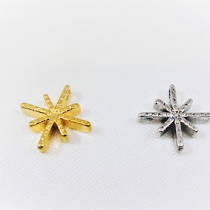 May include: Two star-shaped charms, one gold and one silver. Both charms have a textured surface and eight points.