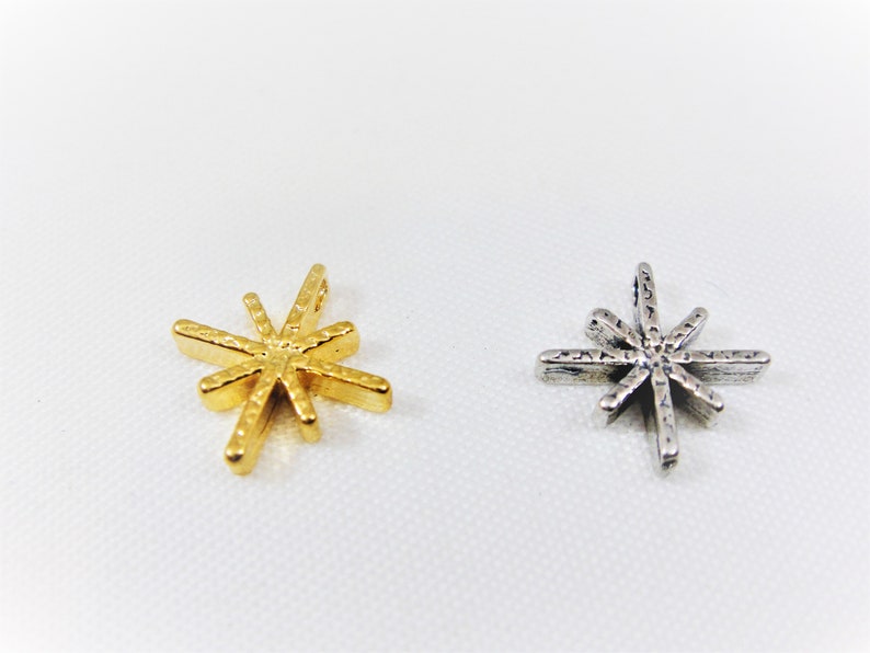 May include: Two star-shaped charms, one gold and one silver. Both charms have a textured surface and eight points.