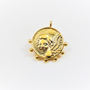 May include: Gold-toned pendant featuring a detailed angel with wings, surrounded by small beads.