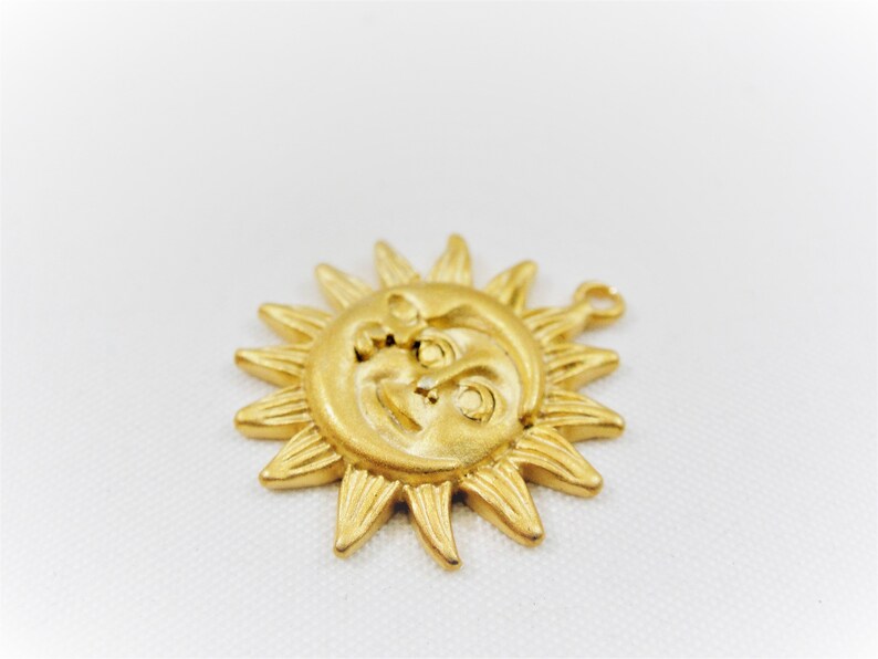 May include: Gold-toned metal sun and moon charm with a face on each. The sun has rays and the moon is a crescent shape.