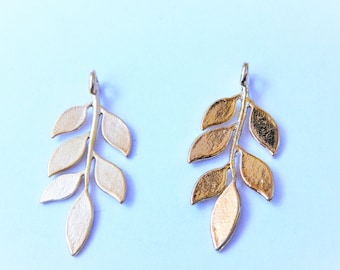 May include: Two gold leaf branch charms with a delicate design. The charms are made of metal and have a shiny finish.