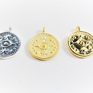 May include: Three round pendants with a raised eye design and star accents. The pendants are silver, gold, and gold.