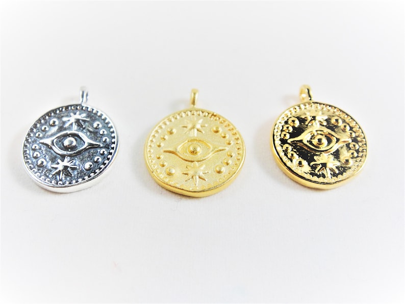 May include: Three round pendants with a raised eye design and star accents. The pendants are silver, gold, and gold.