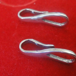 May include: Two silver-toned metal clasps with a loop on one end and a hook on the other. The clasps are on a red surface.