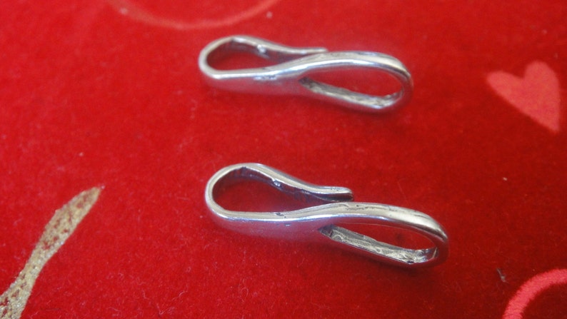 May include: Two silver-toned metal clasps with a loop on one end and a hook on the other. The clasps are on a red surface.