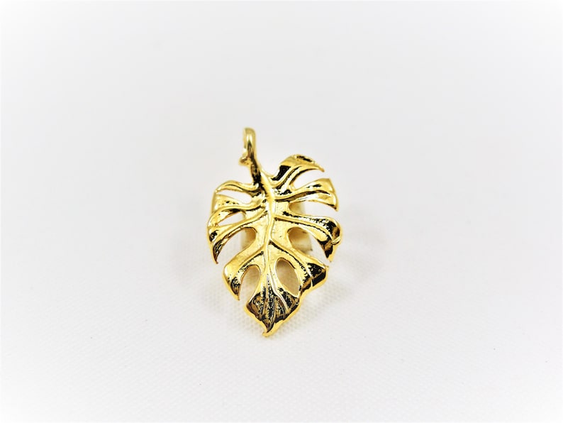 May include: A gold-colored metal pendant shaped like a monstera leaf.