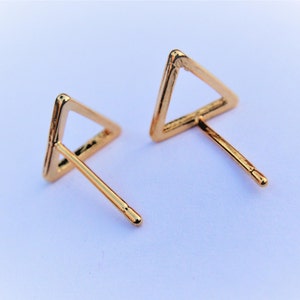 May include: A pair of gold triangle stud earrings. The earrings are simple and minimalist, with a thin wire frame.