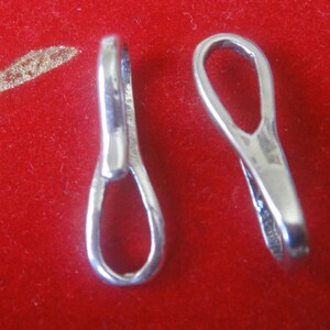 May include: Two silver-toned metal jewelry clasps, each with a loop on one end and a small opening on the other end. The clasps are on a red background.