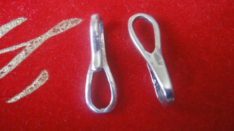 May include: Two silver-toned metal jewelry clasps, each with a loop on one end and a small opening on the other end. The clasps are on a red background.