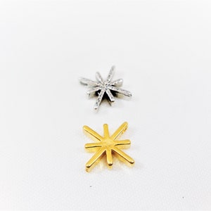 May include: Two star-shaped charms, one silver and one gold. Both charms have eight points.