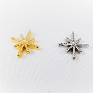 May include: Two star-shaped charms, one gold and one silver. Both charms have a textured surface and a pointed design.