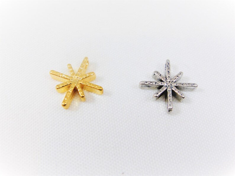 May include: Two star-shaped charms, one gold and one silver. Both charms have a textured surface and a pointed design.