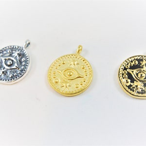 May include: Three round pendants with an eye design and star accents. The pendants are silver, gold, and gold with a black background.
