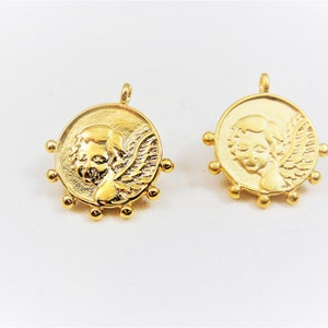 May include: Two gold-toned metal charms featuring a cherub with wings. Each charm has a circular design with a beaded border.