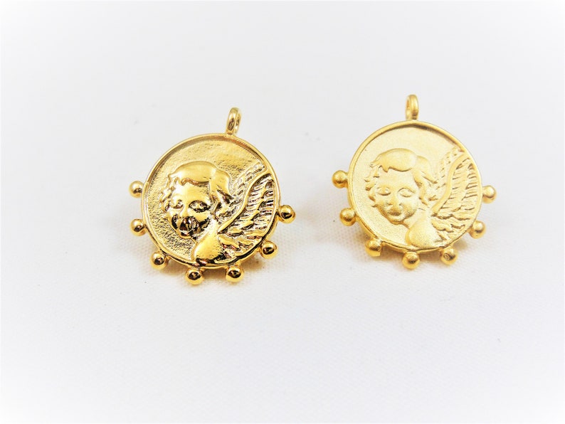 May include: Two gold-toned metal charms featuring a cherub with wings. Each charm has a circular design with a beaded border.