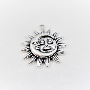 May include: Silver charm featuring a sun and moon design. The sun has a face and the moon is crescent shaped.