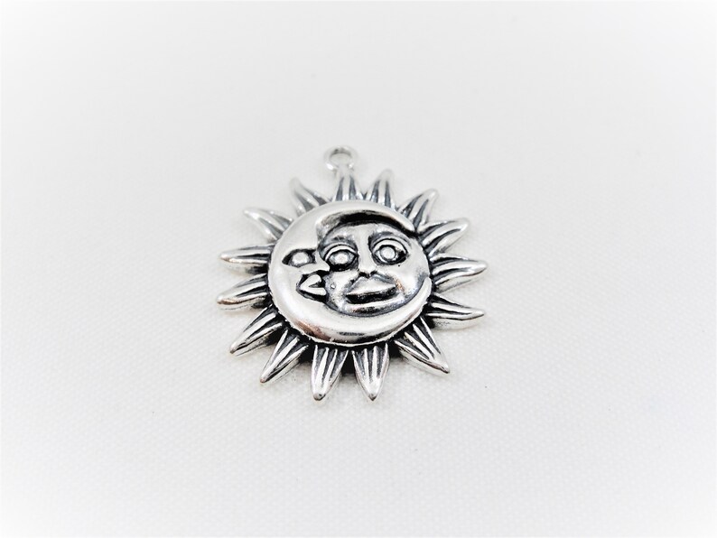 May include: Silver charm featuring a sun and moon design. The sun has a face and the moon is crescent shaped.