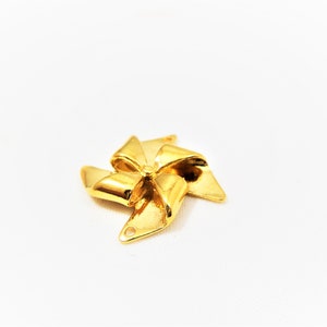 May include: Gold-colored metal charm shaped like a pinwheel with five points. The charm has a hole at the top for attaching to a necklace or bracelet.