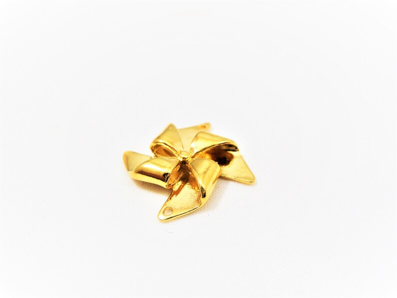 May include: Gold-colored metal charm shaped like a pinwheel with five points. The charm has a hole at the top for attaching to a necklace or bracelet.