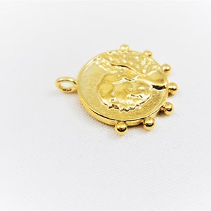 May include: Gold-toned pendant featuring a detailed profile of a person's face with a textured background. The pendant is surrounded by a circle of small gold beads.