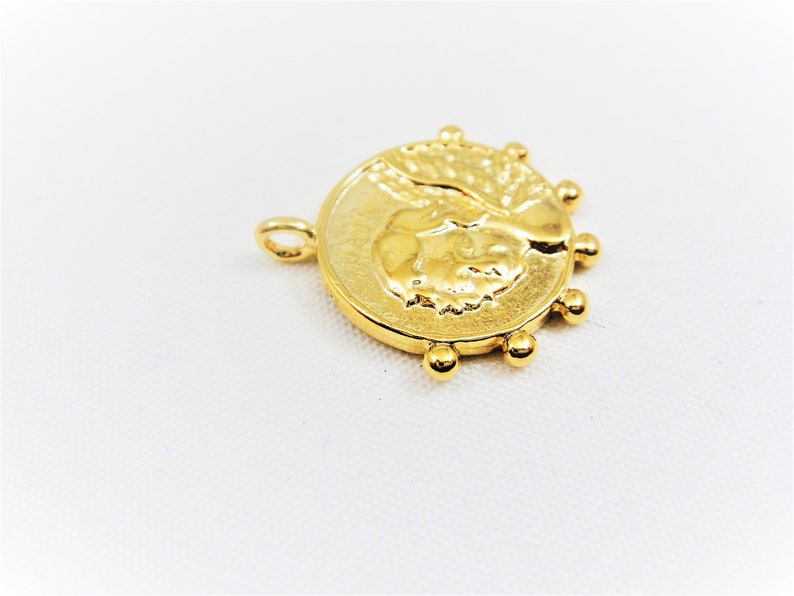 May include: Gold-toned pendant featuring a detailed profile of a person's face with a textured background. The pendant is surrounded by a circle of small gold beads.