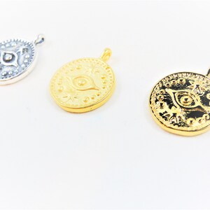 May include: Three gold and silver pendants with an evil eye design. The pendants are round and have a detailed design with a raised eye in the center.