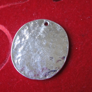 May include: A silver round pendant with a hammered texture and a hole at the top for hanging.