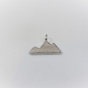 May include: Silver mountain charm pendant. The charm is shaped like a mountain range with three peaks.