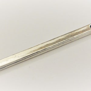 May include: A silver metal bar with a small hole at one end. The bar has a slightly textured surface.