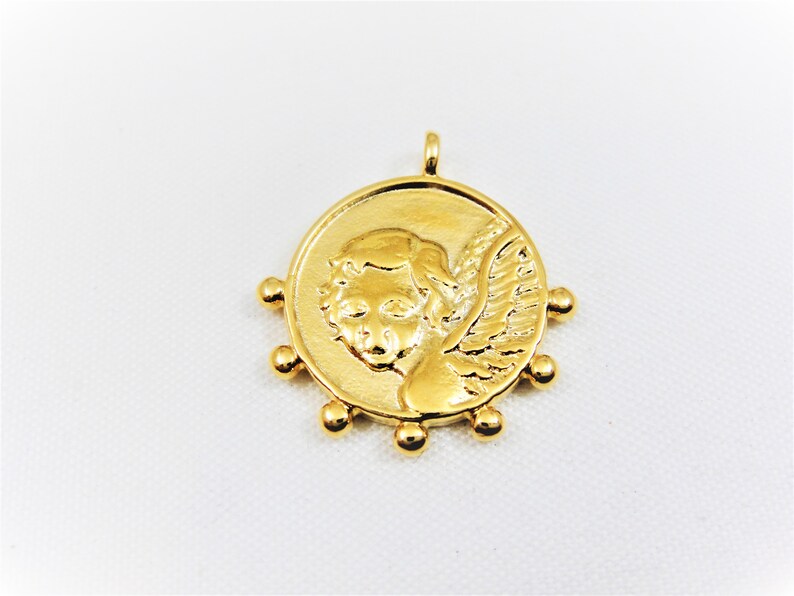 May include: Gold-toned pendant featuring a cherub with wings, surrounded by small beads.