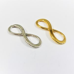 Könnte beinhalten: Zwei Unendlichkeits-Anhänger, einer in Silber und einer in Gold. Die Anhänger sind beide etwa 2,5 cm lang und haben eine glatte, abgerundete Oberfläche.