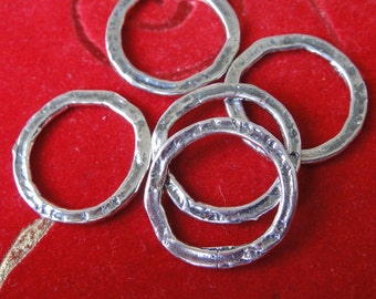 May include: Five silver jump rings with a hammered texture. The rings are arranged in a pile on a red velvet surface.