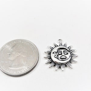 May include: Silver charm featuring a sun and moon design. The sun has a face and the moon is a crescent shape. The charm is about the size of a US quarter.