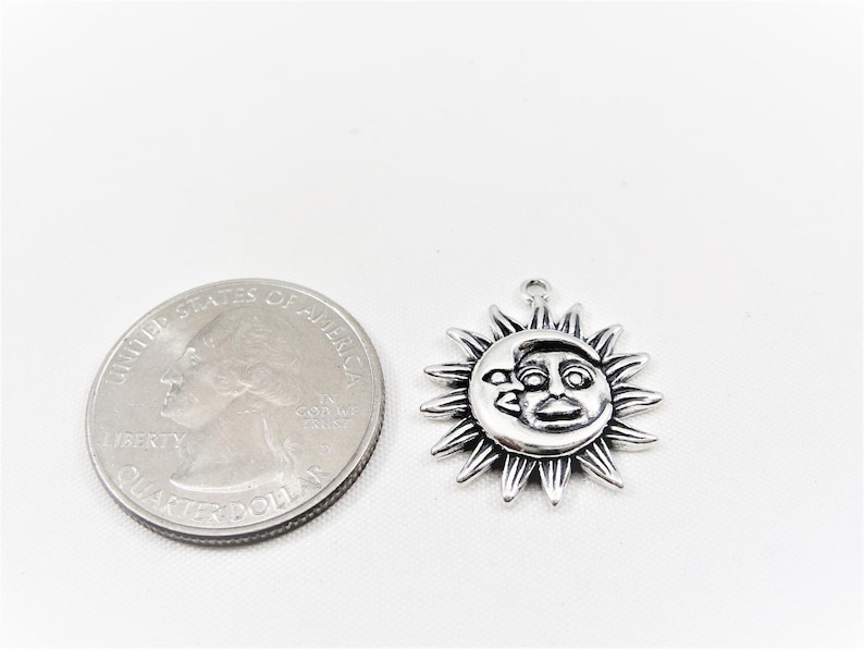 May include: Silver charm featuring a sun and moon design. The sun has a face and the moon is a crescent shape. The charm is about the size of a US quarter.