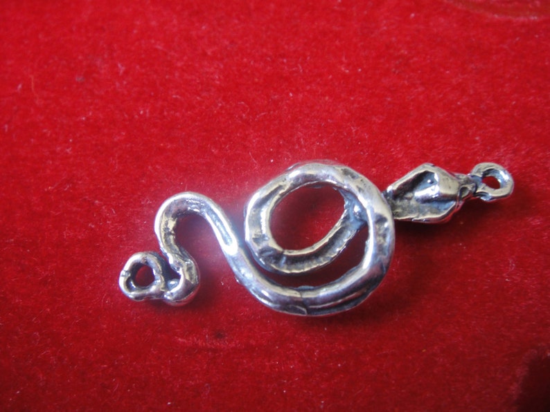 Peut inclure: Un charme en argent en forme de serpent avec un corps enroul&eacute; et une t&ecirc;te relev&eacute;e. Le charme a une surface textur&eacute;e et une boucle pour l'attacher &agrave; un bracelet ou un collier.