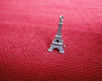 May include: A silver charm in the shape of the Eiffel Tower. The charm is small and detailed, with a loop at the top for attaching to a bracelet or necklace.