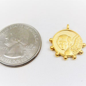 May include: Gold-toned pendant featuring a cherub with wings, surrounded by small beads. The pendant is about the size of a UK 20 pence coin.