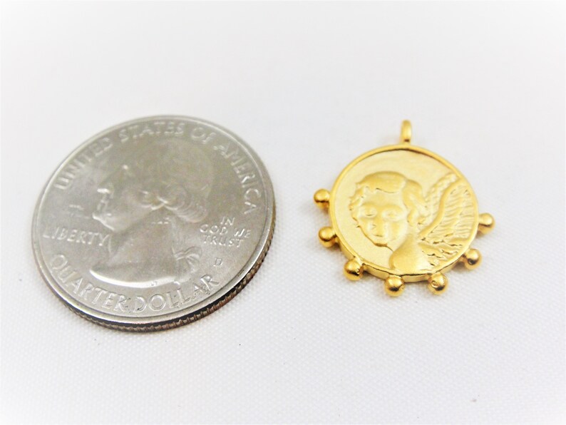 May include: Gold-toned pendant featuring a cherub with wings, surrounded by small beads. The pendant is about the size of a UK 20 pence coin.