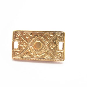 Peut inclure: Une pièce décorative rectangulaire en métal doré avec des motifs floraux complexes et un carré central. La pièce a deux petits trous sur les côtés.