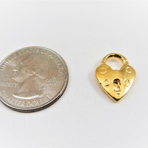 以下が含まれることがあります： 鍵穴のある金色のハート型の南京錠チャーム。チャームはアメリカの25セント硬貨と同じくらいの大きさです。