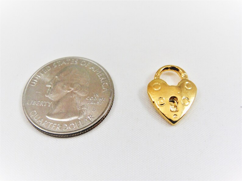 以下が含まれることがあります： 鍵穴のある金色のハート型の南京錠チャーム。チャームはアメリカの25セント硬貨と同じくらいの大きさです。