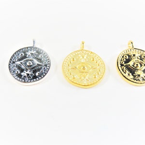 May include: Three round pendants with an eye design and star-shaped accents. The pendants are silver, gold, and gold.