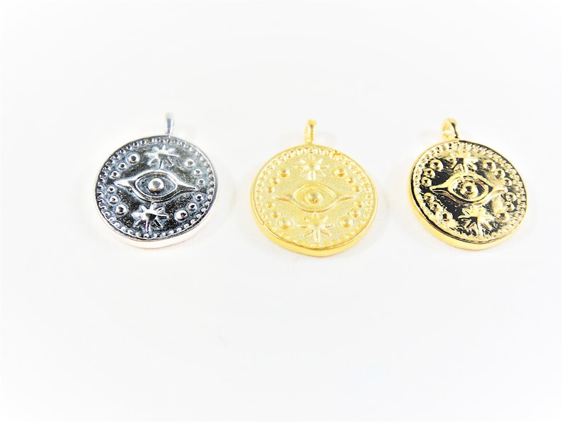 May include: Three round pendants with an eye design and star-shaped accents. The pendants are silver, gold, and gold.